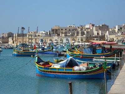 Bunte Fischerboote vor der Kulisse eines maltesischen Dorfes.